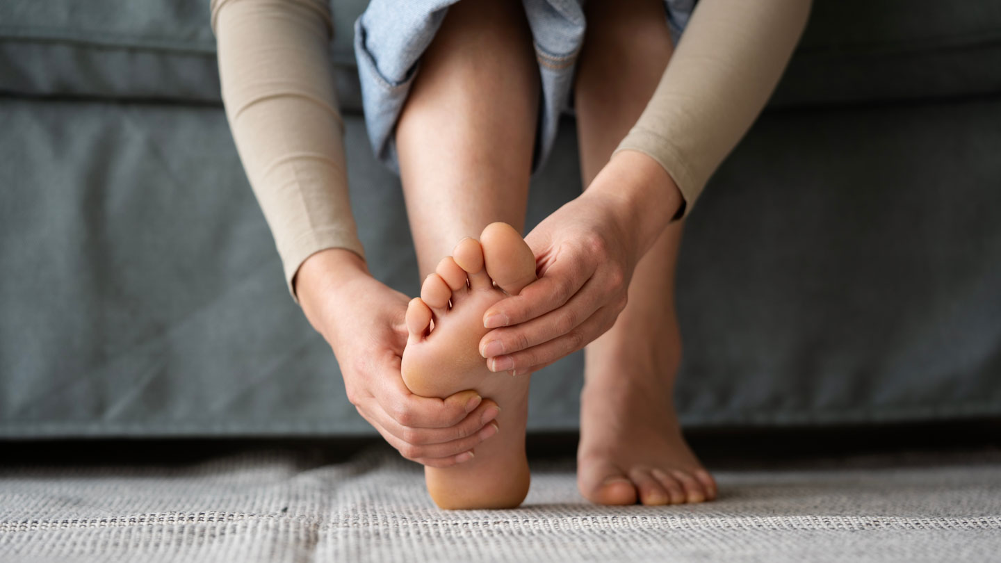 Person sitting on a couch holding their foot, indicating foot pain or discomfort.