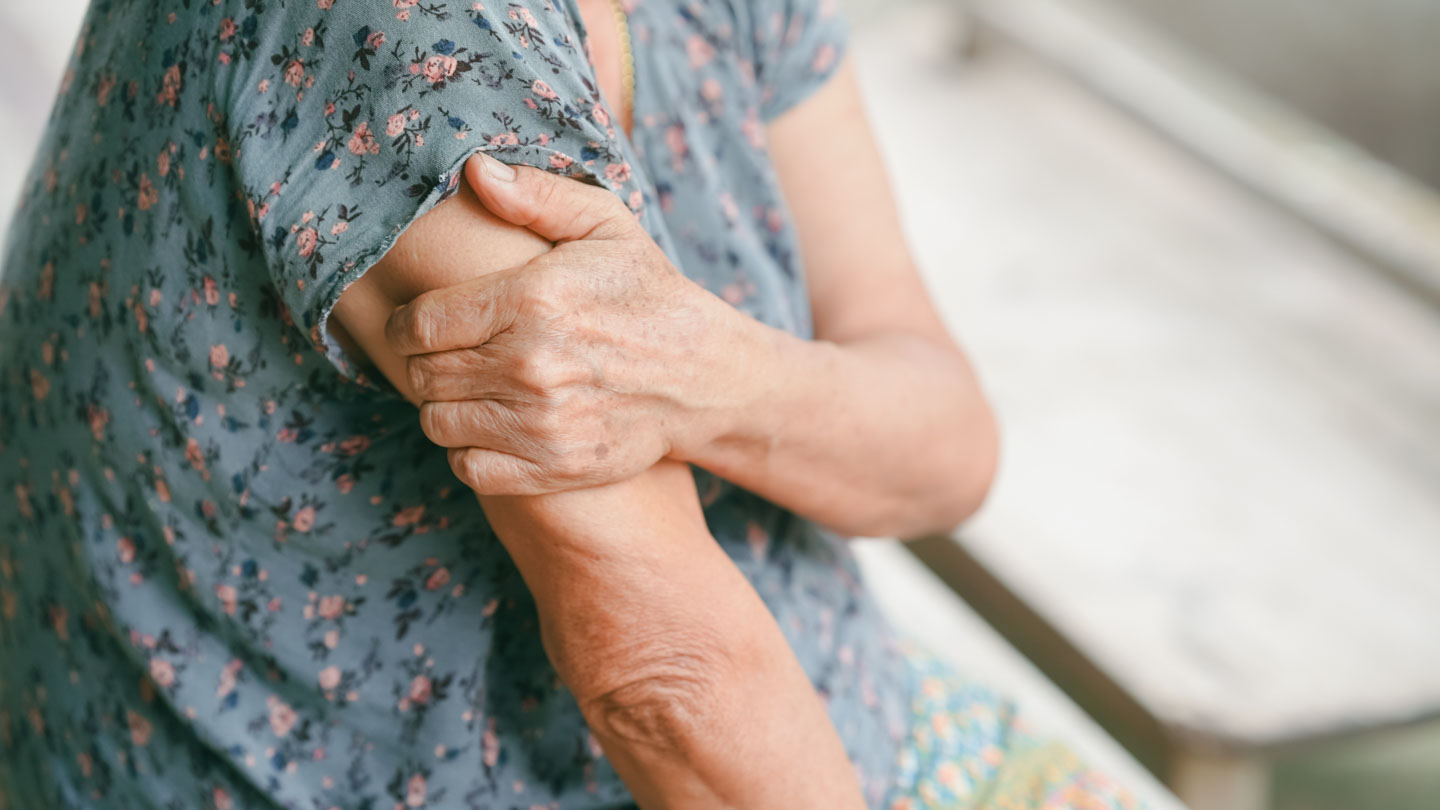Elderly person holding their upper arm, possibly showing muscle weakness or pain.