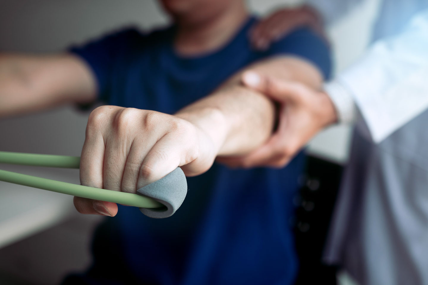 A person exercises arm with resistance band while a healthcare provider supports the arm.