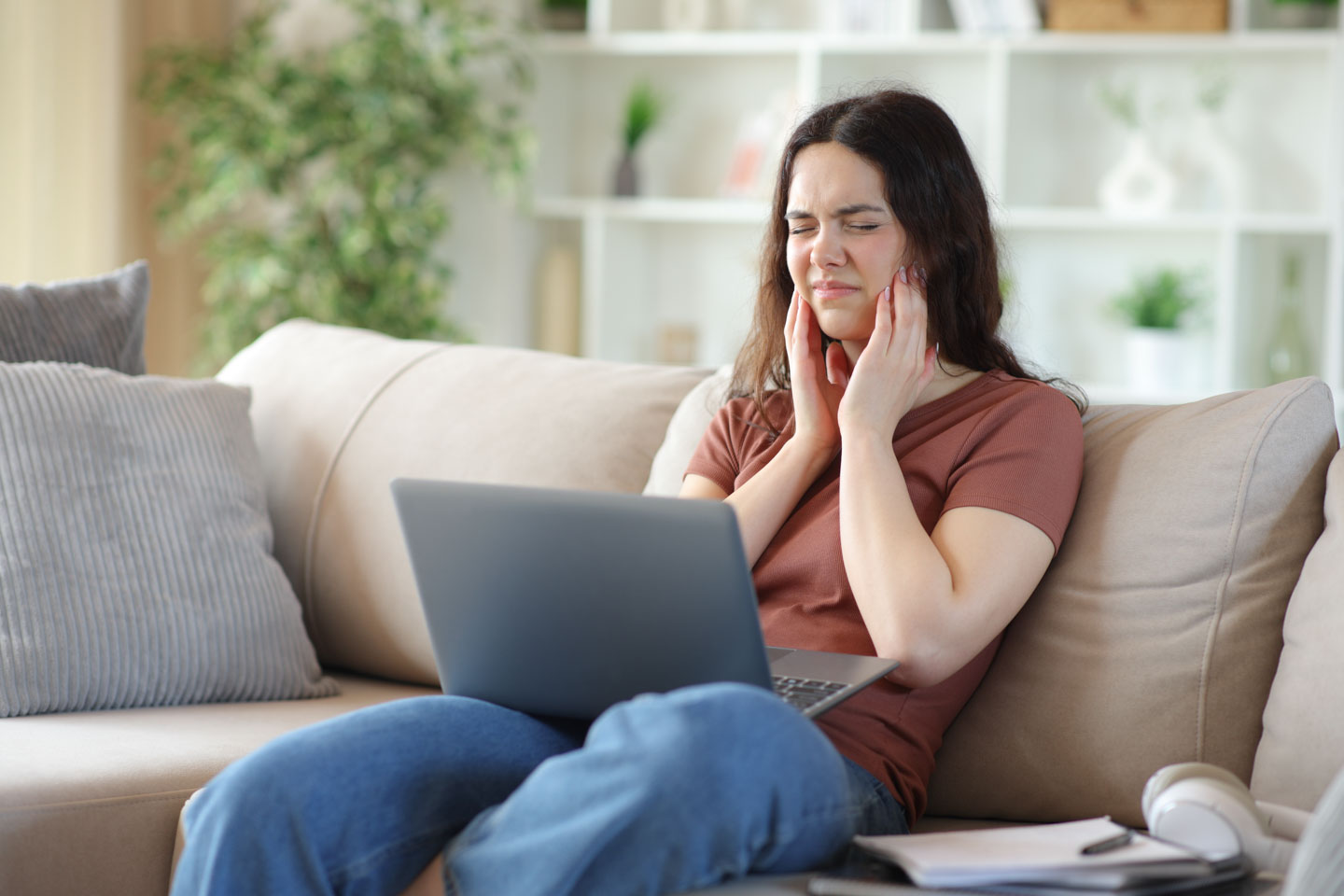 woman on a couch, touching her jaw in pain